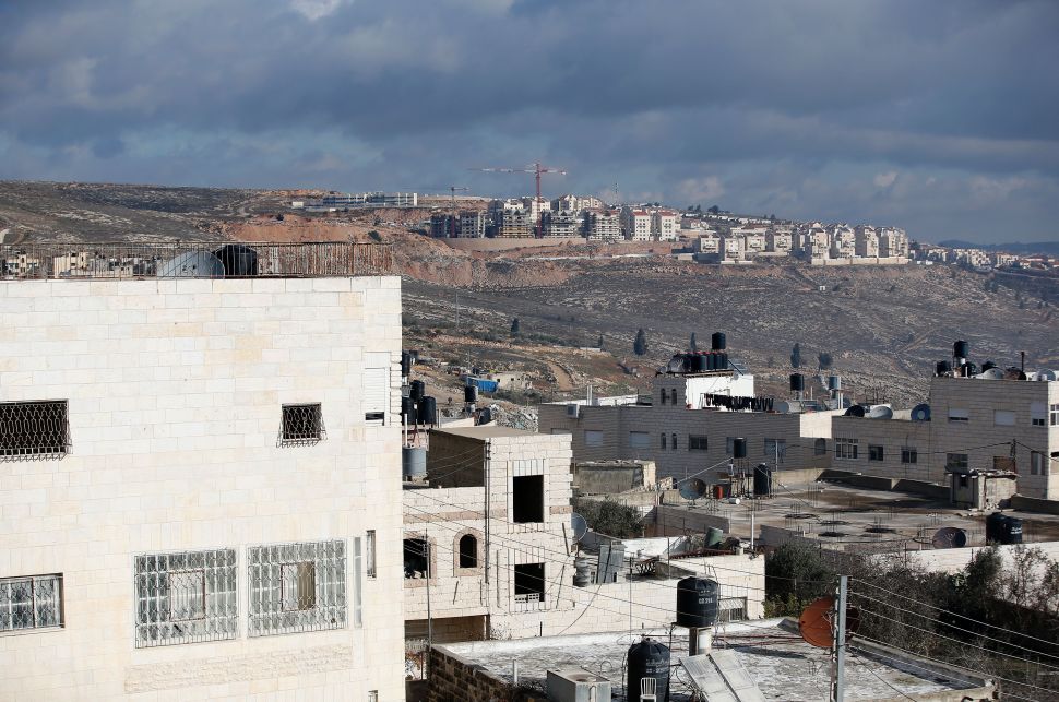 A picture taken on January 3, 2017 shows Israeli construction cranes and excavators at a building site of new housing units in the Jewish settlement of Kochav Ya'akov near the West Bank city of Ramallah (top), adjacent to Qalandiya refugee camp. / AFP / AHMAD GHARABLI (Photo credit should read