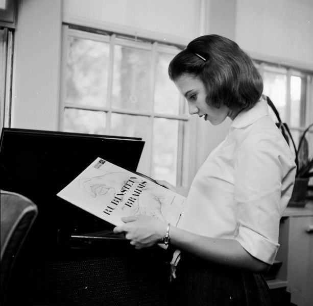 circa 1955: A teenage girl studying a record cover before playing the record inside it. (Photo by 