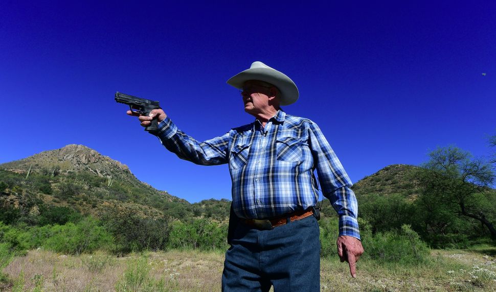 Jim Chilton carries his Smith and Wesson pistol for protection as he approaches the US-Mexico border at his ranch some 20 miles southeast of Arivaca, Arizona on October 14, 2016. Chilton owns a 50,000-acre (20234-hectare) cattle ranch where illegals but mostly drug packers have been crossing easily for many years. / AFP / Frederic J. BROWN