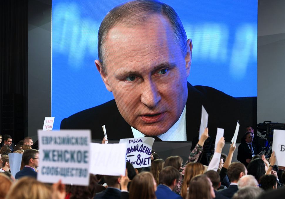 TOPSHOT - A video screen displays Russian President Vladimir Putin speaking during his annual press conference in Moscow while journalists hold the name of their media, on December 23, 2016. / AFP / Natalia KOLESNIKOVA (Photo credit should read