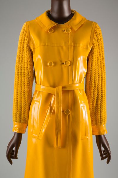 Double breasted coat in bright yellow vinyl plastic; open round neck with peter pan collar; plastic cuffs. Matching tie belt.