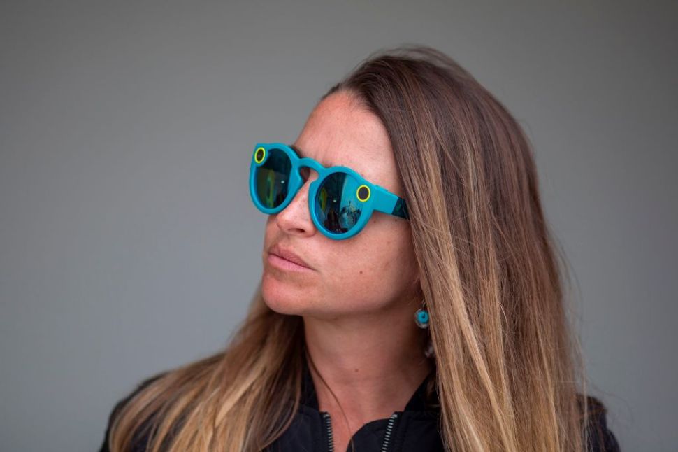 A woman wears Spectacles as residents demonstrate near a building converted into a Snap, Inc., vender of Spectacles sunglass cameras for Snapchat, on the Venice Beach boardwalk on March 11, 2017 in the Venice area of Los Angeles, California. Protesters accuse Snap of buying up residential and small business buildings throughout Venice and adjacent Marina del Rey, then converting them into commercial offices as a kind of sprawling campus as part of the so-called Silicon Beach movement. / AFP PHOTO / DAVID MCNEW (Photo credit should read DAVID MCNEW/AFP/Getty Images)