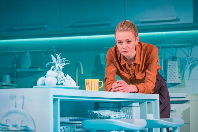 Carey Mulligan leans on a kitchen counter against a blue background in the off-broadway play Girls and Boys.