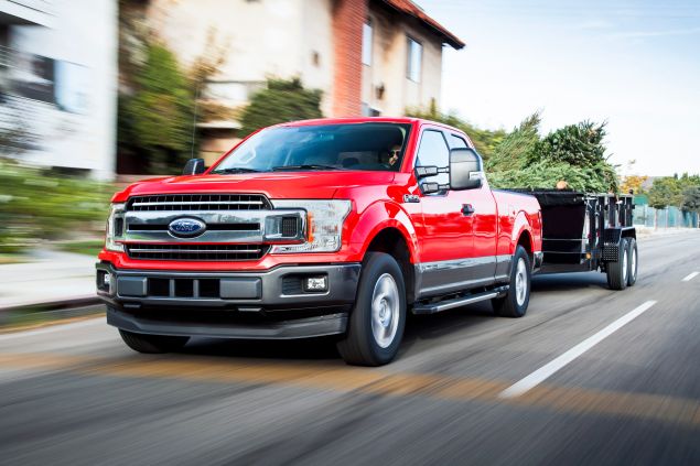 A red 2018 Ford F-150 tows a trailer full of Christmas trees.