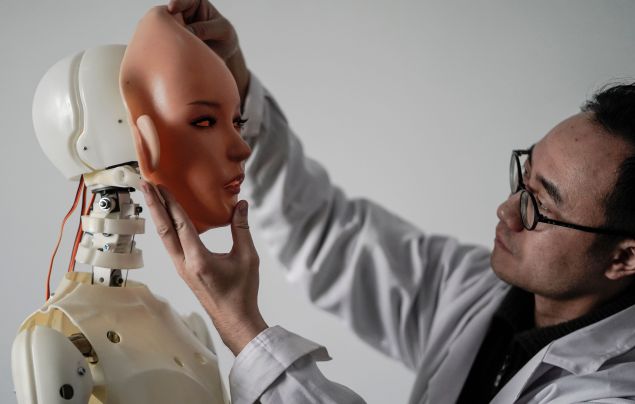 This photo taken on February 1, 2018 shows an engineer holding a silicon face against the head of a robot at a lab of a doll factory of EXDOLL, a firm based in the northeastern Chinese port city of Dalian. With China facing a massive gender gap and a greying population, a company wants to hook up lonely men and retirees with a new kind of companion: "Smart" sex dolls that can talk, play music and turn on dishwashers.
