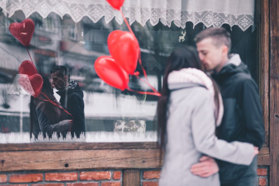 A man and woman kiss with red balloons.