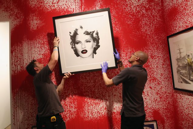 Sotheby's employees hang a print ahead of the first unauthorized retrospective of works by UK artist Banksy on June 6, 2014, curated by Steve Lazarides.