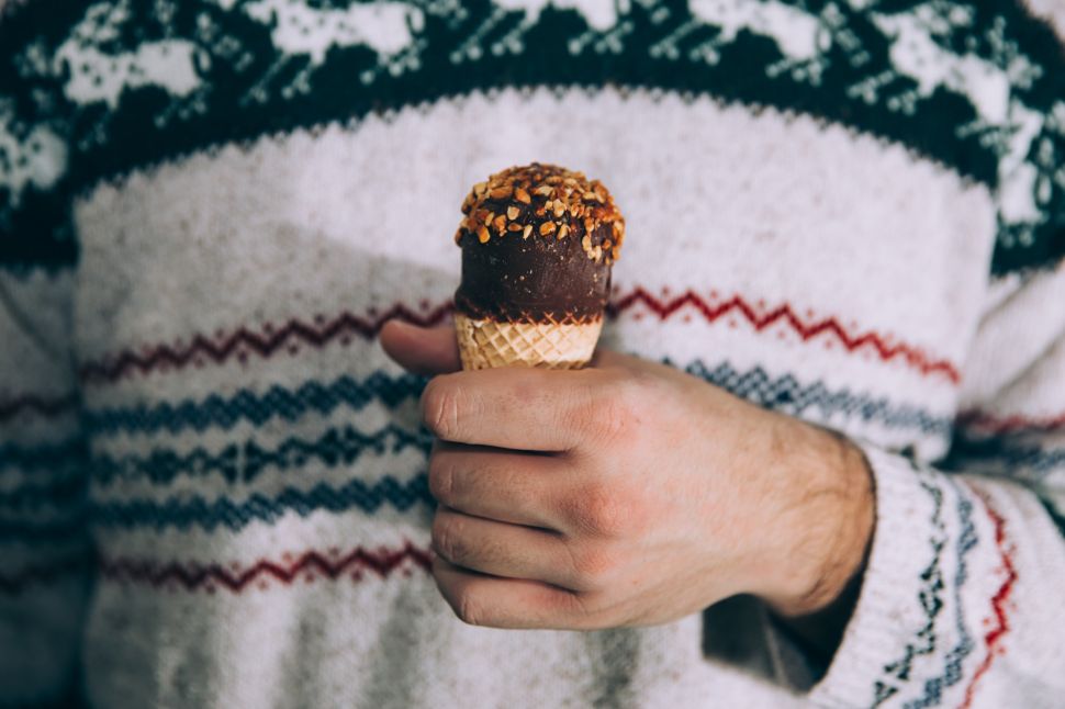 A man wearing a festive winter sweater holds an ice cream cone.