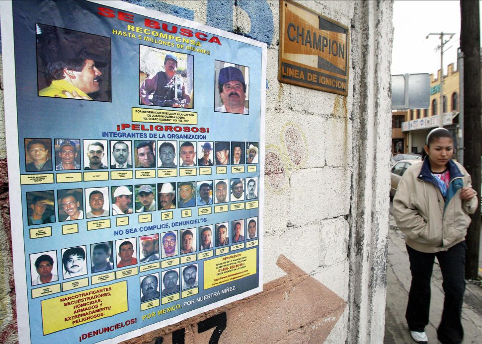 A woman walks past a poster offering rewards of up to $5 million for information leading to the arrest of 36 members of the Sinaloa Cartel.