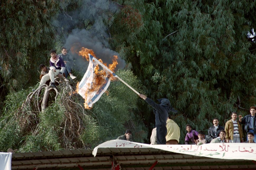 A member of the Palestinian Islamic movement Hamas burns the Israeli flag on the roof of a building during a rally in Gaza City on January 12, 1996.