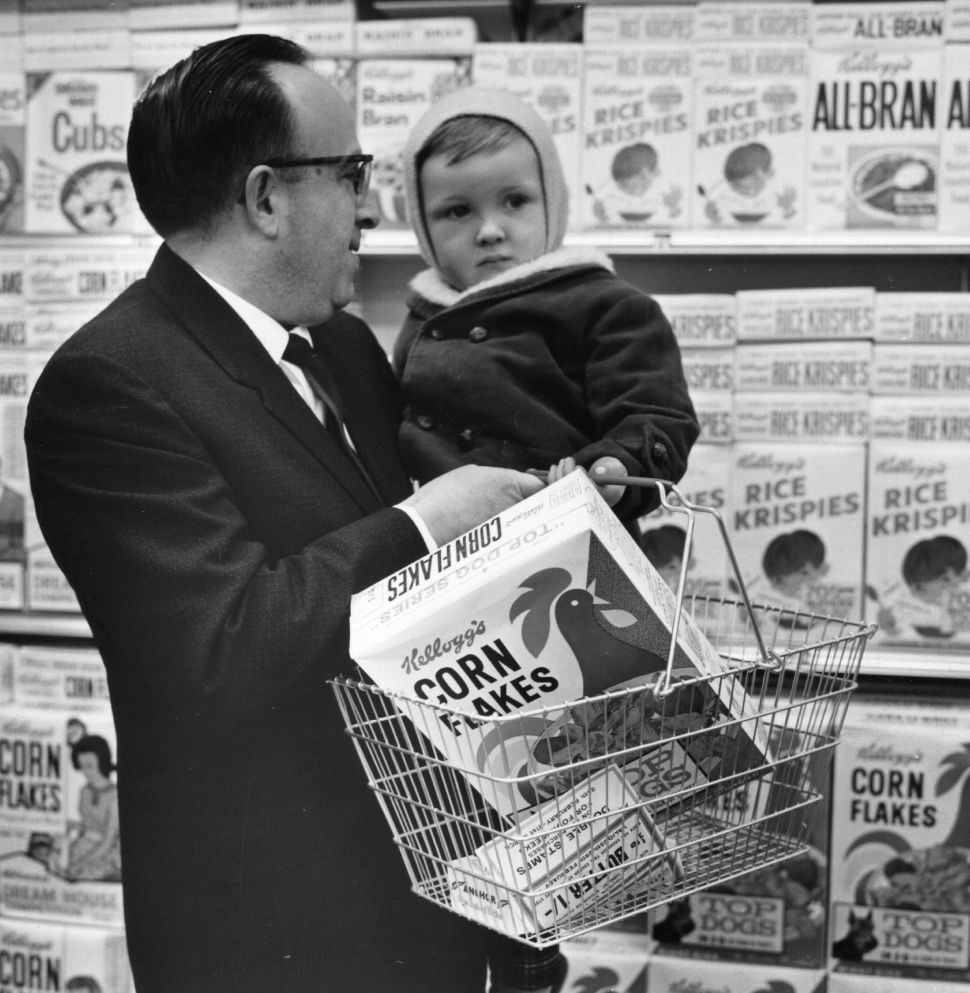 A father holds his baby and Kellogg's Cornflakes, whilst shopping at a Foodtown Supermarket in Lewisham, London on March 4, 1974.