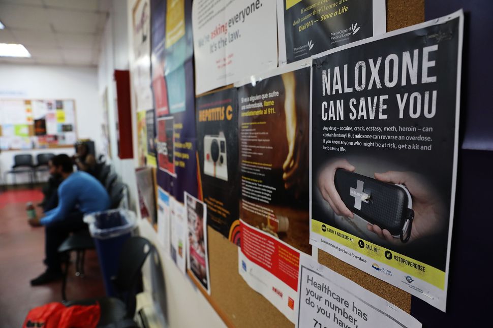 A sign for naloxone hangs on a wall as students learn to put together a naloxone spray gun in a class on opioid overdose prevention.