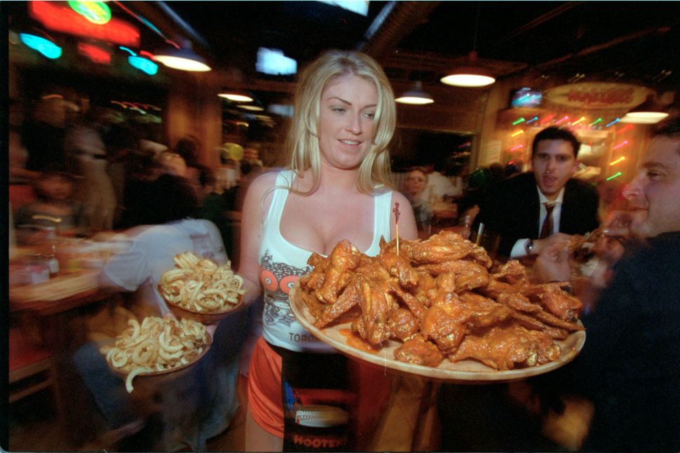 A Hooters waitress serves a large platter of chicken wings.