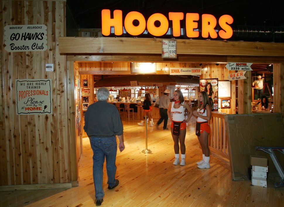 A man enters a Hooters restaurant as waitstaff greet him at the door.