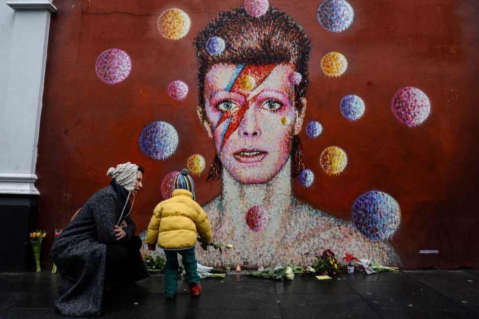 Floral tributes are left beneath a mural of British singer David Bowie, painted by Australian street artist James Cochran (AKA Jimmy C), following the announcement of Bowie's death, in London on January 11, 2016.
