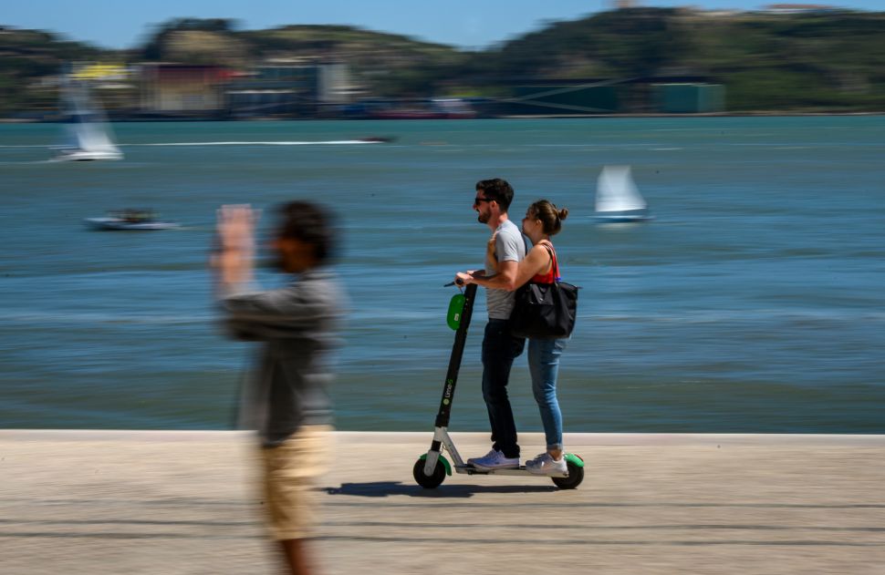 A couple ride an e-scooter—sans helmets and dangerously close to the Tagus River—on June 12, 2019 in Lisbon, Portugal. 